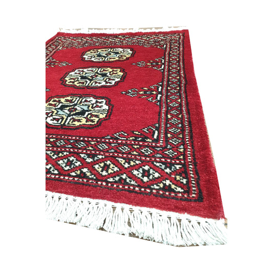 Angled fringe and border detail of Afghan Bokhara wool rug showing red pile, ivory gul motifs and dark geometric edging