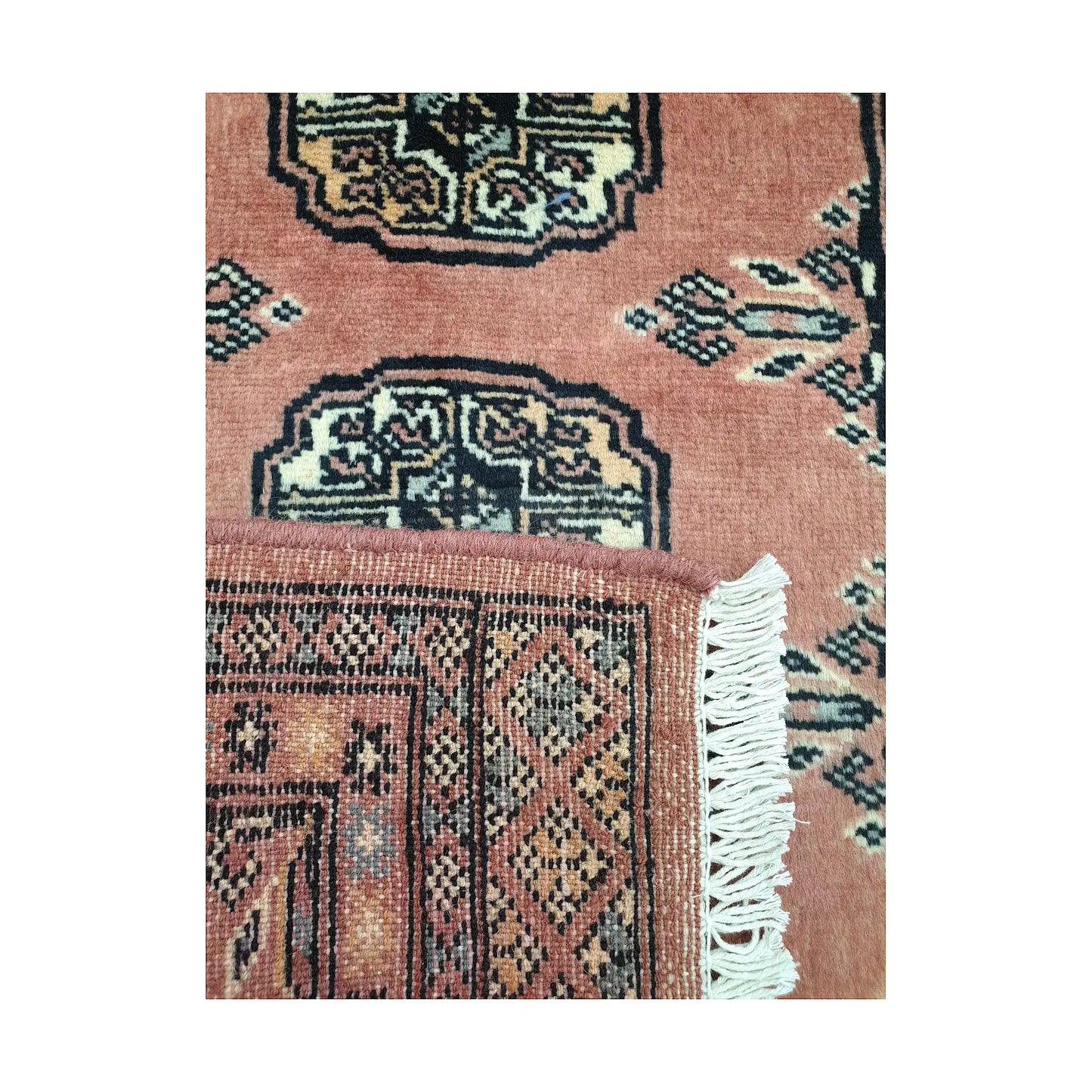 Folded corner detail of Afghan Bokhara wool rug showing the back of the rug, fringe and salmon red front pattern