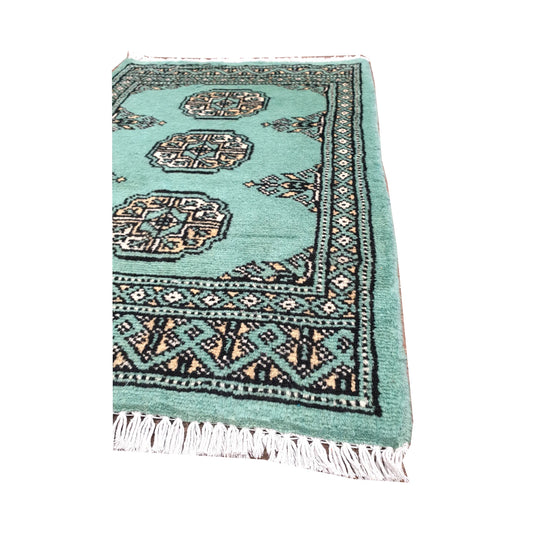 Angled fringe and border detail of Afghan Bokhara wool rug showing light turquoise pile, ivory gul motifs and dark edging