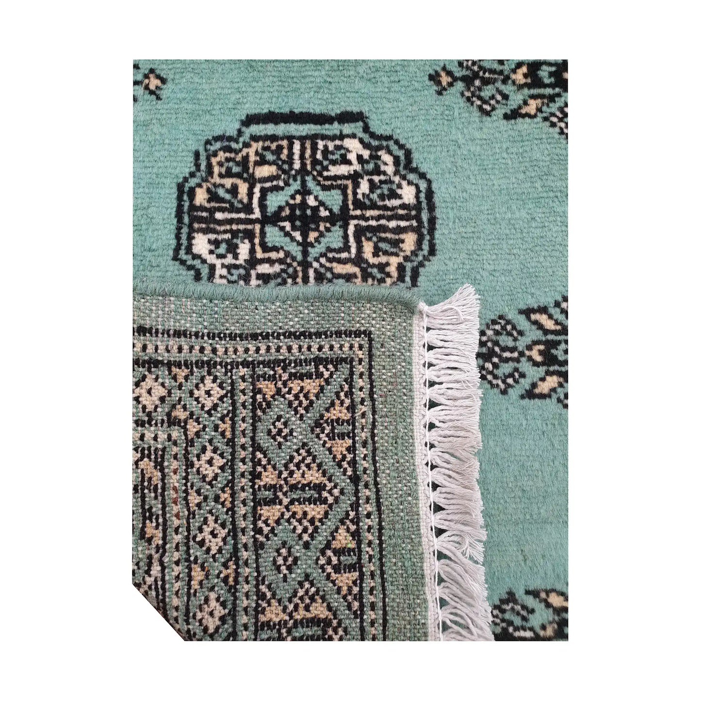 Folded corner detail of Afghan Bokhara wool rug showing the back of the rug, fringe and light turquoise front pattern