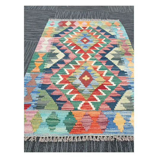 Angled view of Afghan Chobi Kilim flatweave rug showing geometric pastel double diamond pattern, 90 x 64 cm