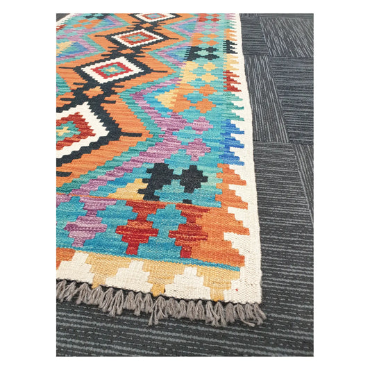 Angled view of Afghan Chobi Kilim runner showing black diamond spine and pastel geometric border, 291 x 80 cm