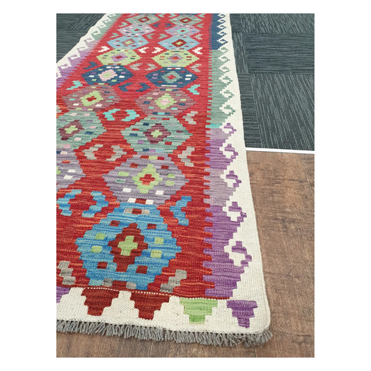 Angled view of Afghan Chobi Kilim runner showing coral geometric medallion pattern and fringe, 386 x 79 cm