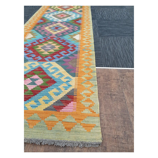 Angled view of Afghan Chobi Kilim runner showing geometric medallion pattern and fringe, 386 x 86 cm