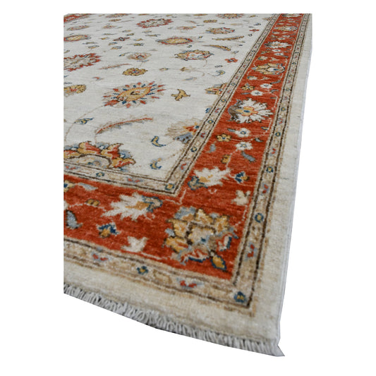 Angled view of Afghan Chobi wool rug showing its off-white floral field, rust-red border and pale fringe