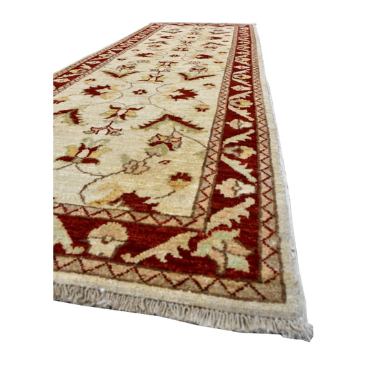 Angled view of Chobi runner showing its red floral border, beige field with curling vines and fringed end