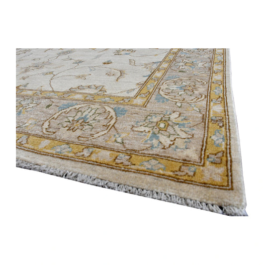 Angled corner detail of Afghan Chobi rug showing the warm tan floral border, pale blue accents and ivory fringe