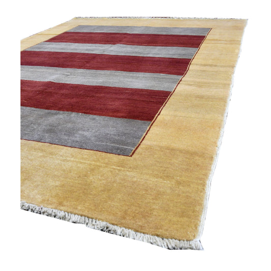 Angled view of Afghan Gabbeh wool rug showing its red and grey striped field, golden-beige border and pale fringe