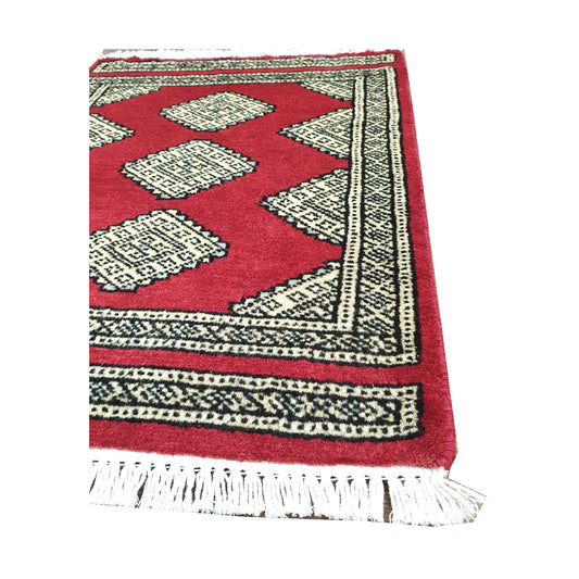 Angled fringe and border detail of Afghan Jaldar wool rug showing red pile, ivory diamond motifs and dark edging
