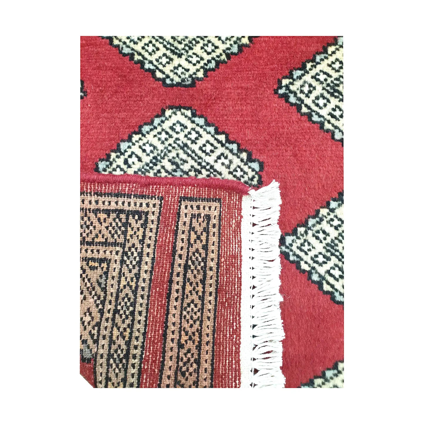 Folded corner detail of Afghan Jaldar wool rug showing the back of the rug, fringe and red front pattern
