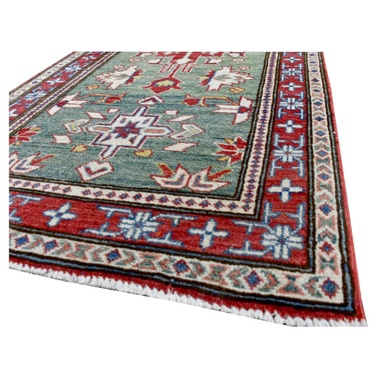 Angled corner and fringe view of Afghan Kazak runner showing the sage-green field, red border and wool pile
