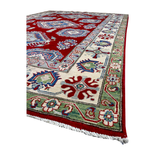 Angled view of Afghan Kazak rug showing its red medallion field, cream patterned border, pale green band and light fringe