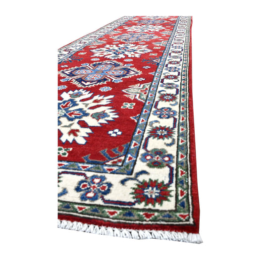 Angled view of Afghan Kazak runner showing its red medallion field, broad ivory floral border and white fringe