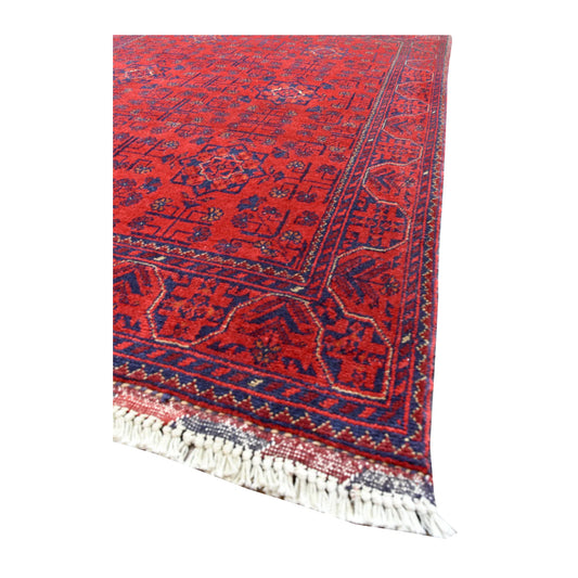 Angled detail of Afghan Khal Mohammadi rug showing its red floral field, navy leaf-patterned border and ivory fringe