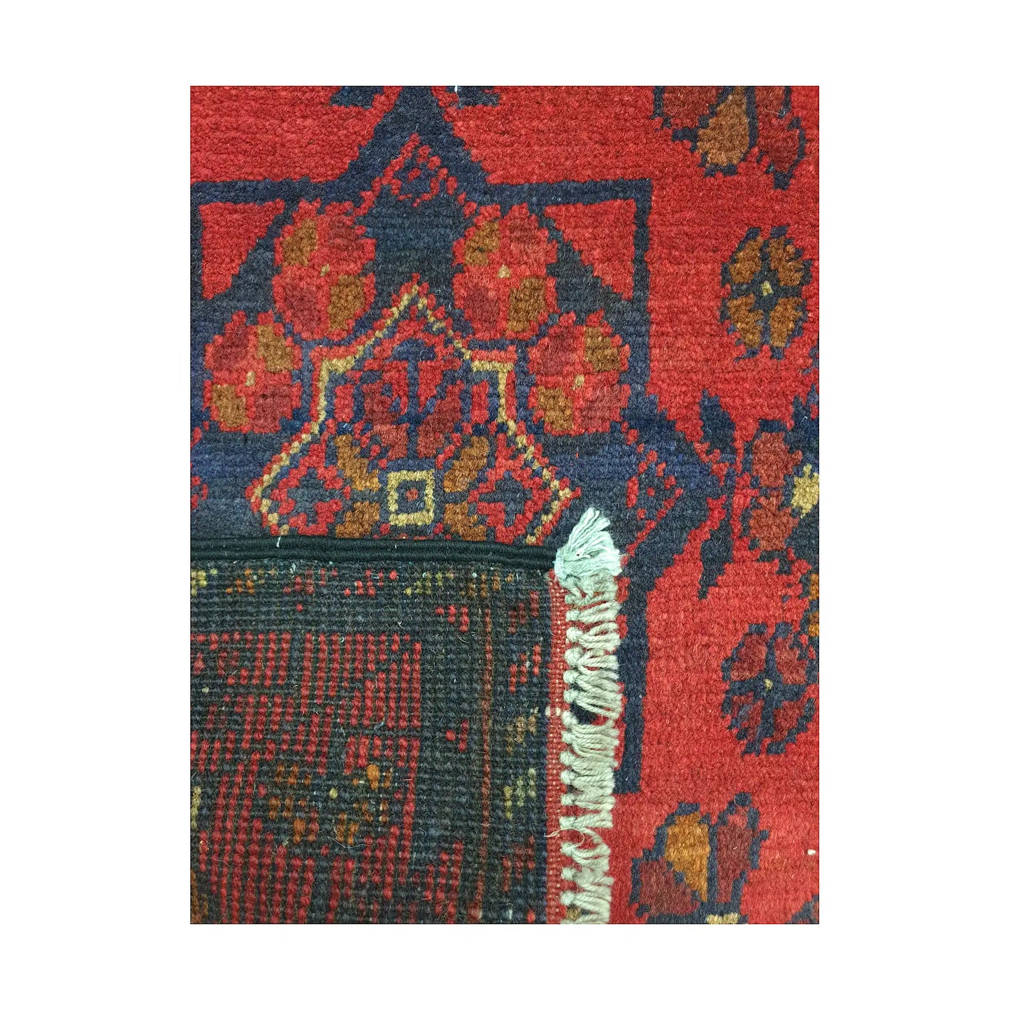 Folded corner detail of Afghan Khal Mohammadi wool rug showing the back, fringe and red front pattern
