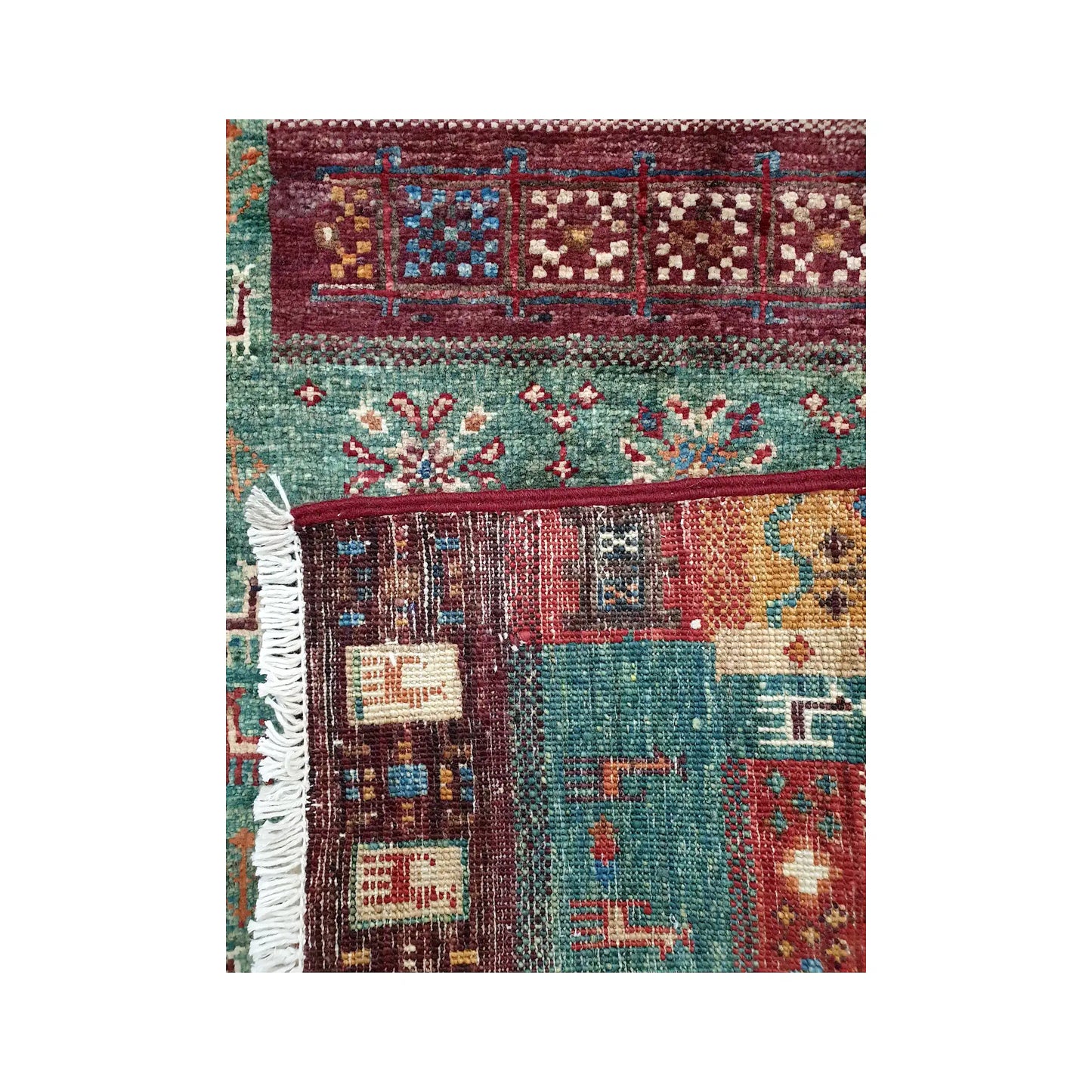 Folded corner detail of Afghan Khurjeen rug showing the back of the rug, fringe and front panel pattern