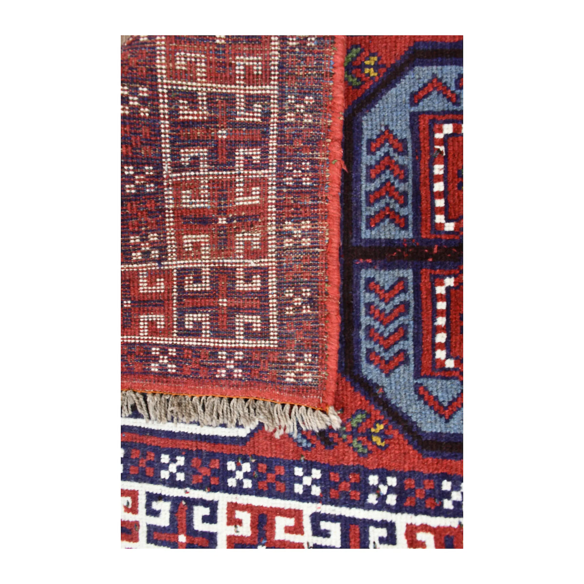 Folded-corner detail of Mashwani rug showing the reverse weave beside the red field and ivory geometric border