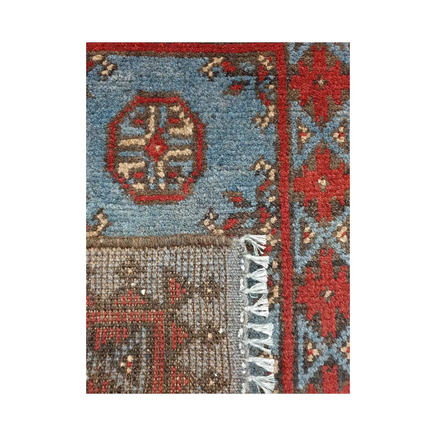 Folded corner detail of Afghan Turkoman blue wool rug showing the back, fringe and blue-red front pattern