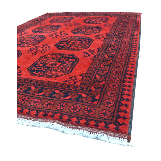 Angled view of Afghan Turkoman rug showing its deep red field, dark octagonal guls, layered geometric borders and pale fringe