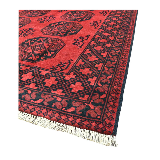 Angled view of Afghan Turkoman rug showing its red field, dark octagonal guls, geometric borders and pale fringe