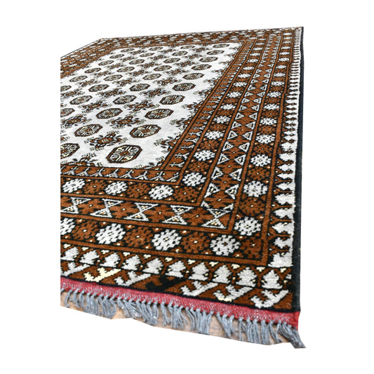 Angled view of Afghan Turkoman rug showing its off-white field, layered warm brown border and blue-grey fringe