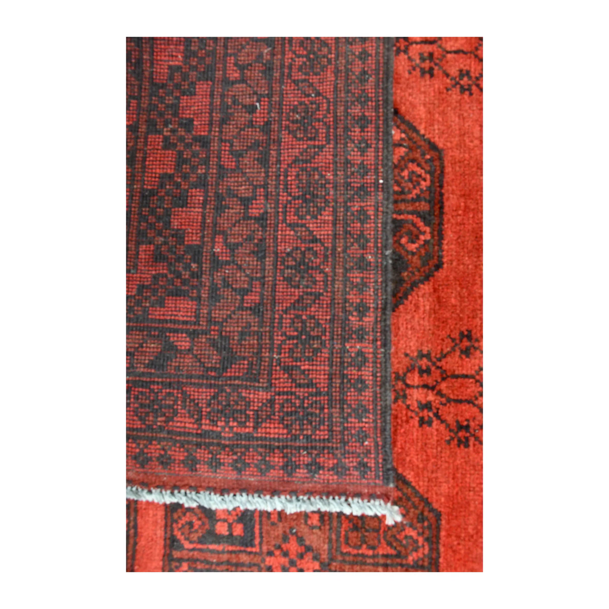 Folded-corner detail of Afghan Turkoman rug showing the reverse weave beside its red front, dark border and white fringe