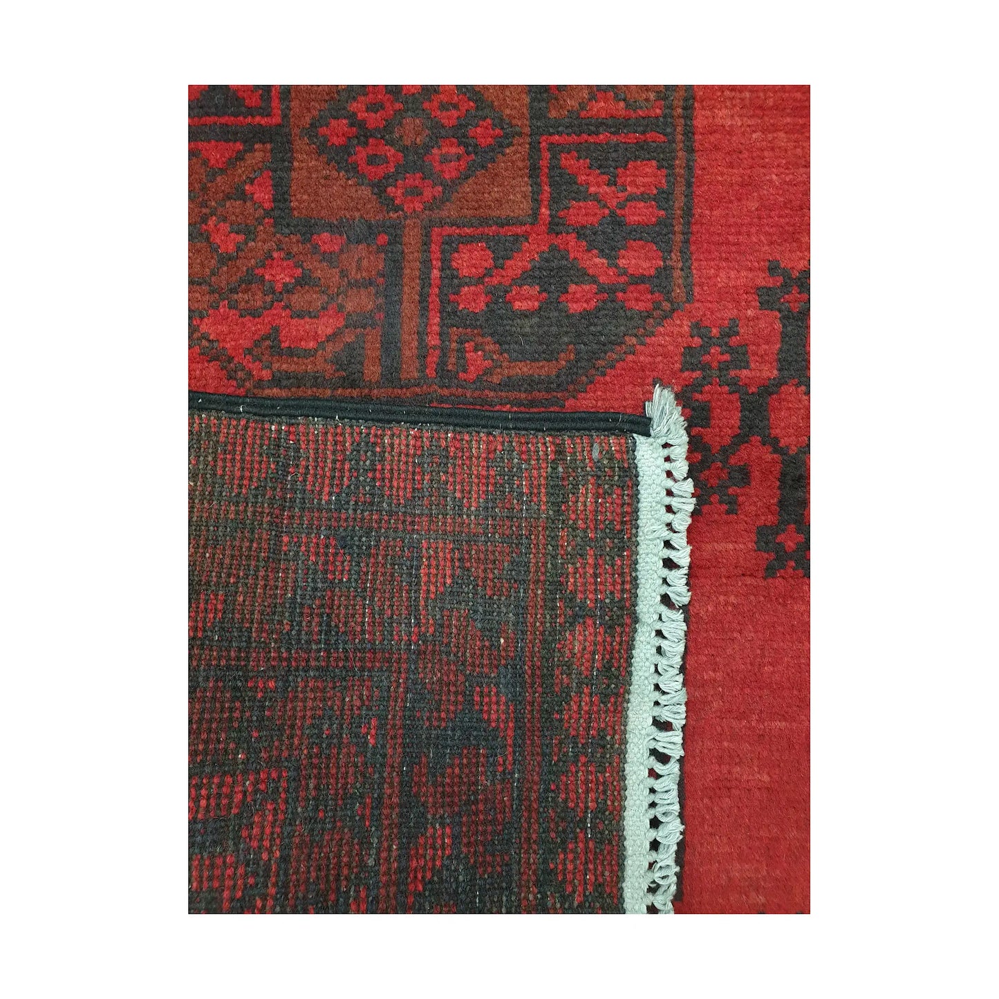 Folded corner detail of Afghan Turkoman rug showing the back of the rug, fringe and red front pattern