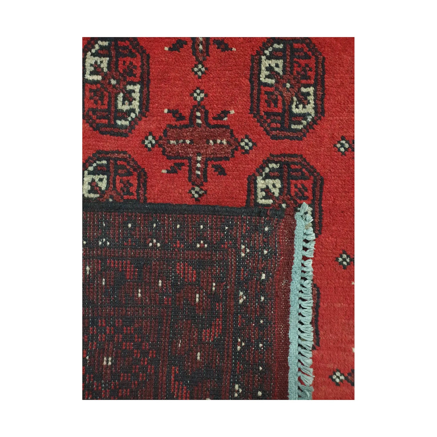 Folded corner detail of Afghan Turkoman rug showing the back of the rug, fringe and red front pattern
