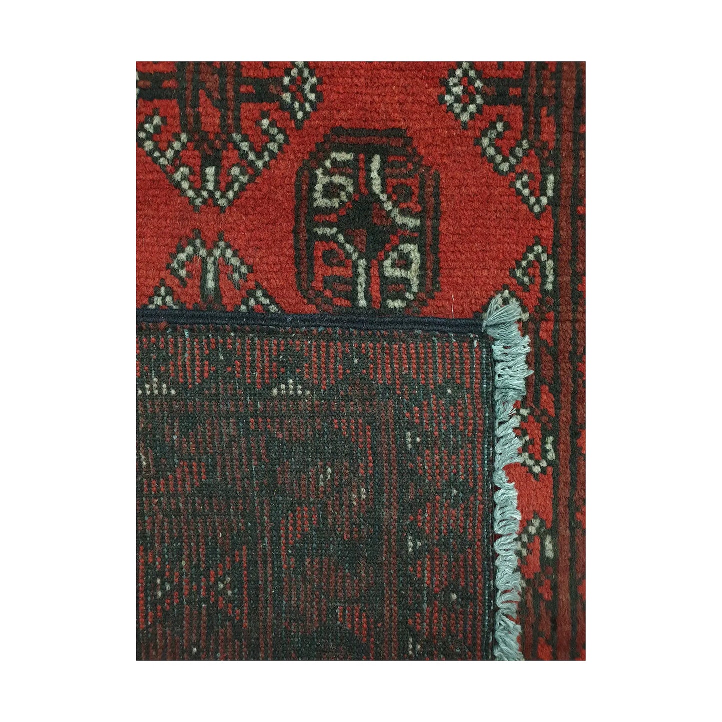 Folded corner detail of Afghan Turkoman rug showing the back of the rug, fringe and red front pattern
