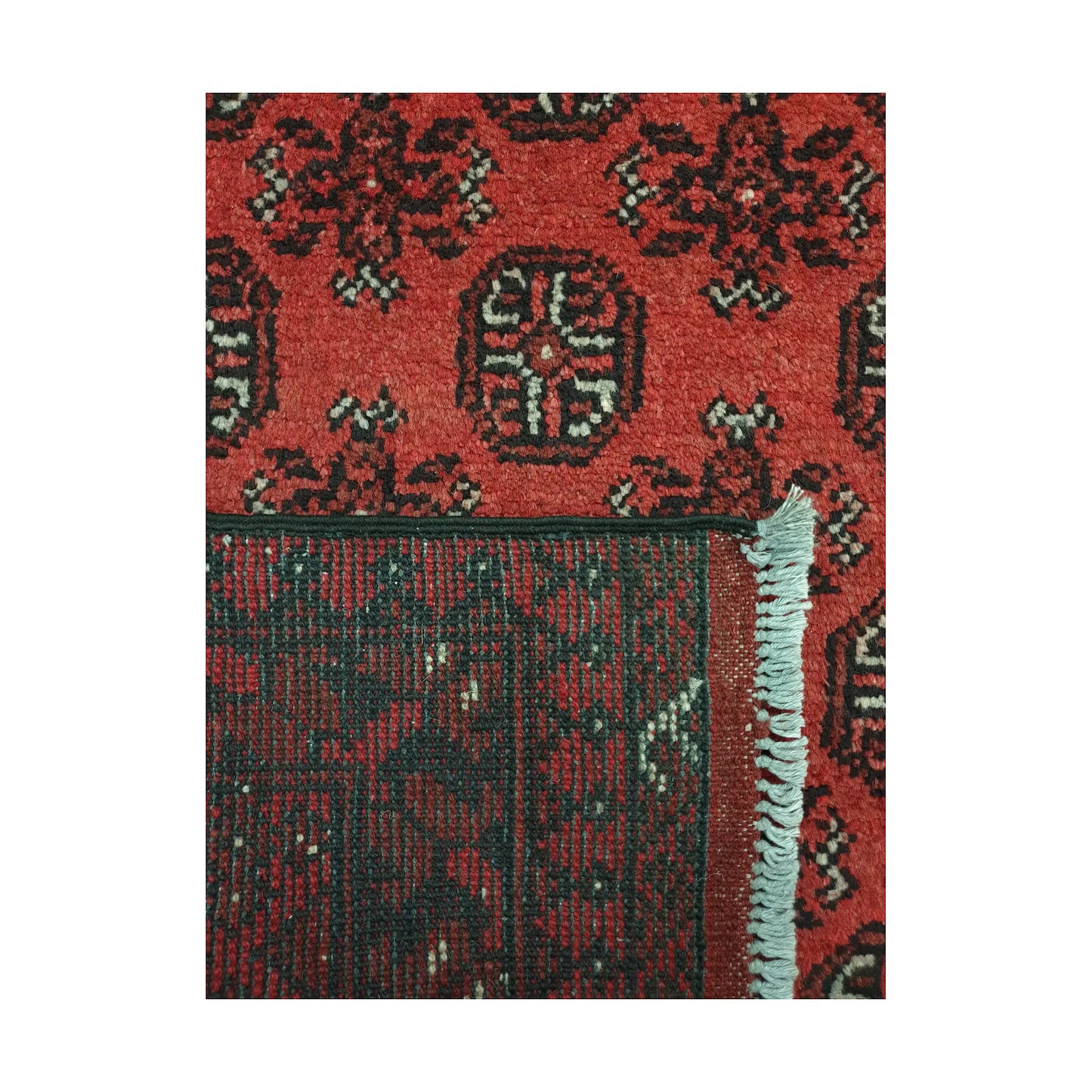 Folded corner detail of Afghan Turkoman rug showing the back of the rug, fringe and red front pattern
