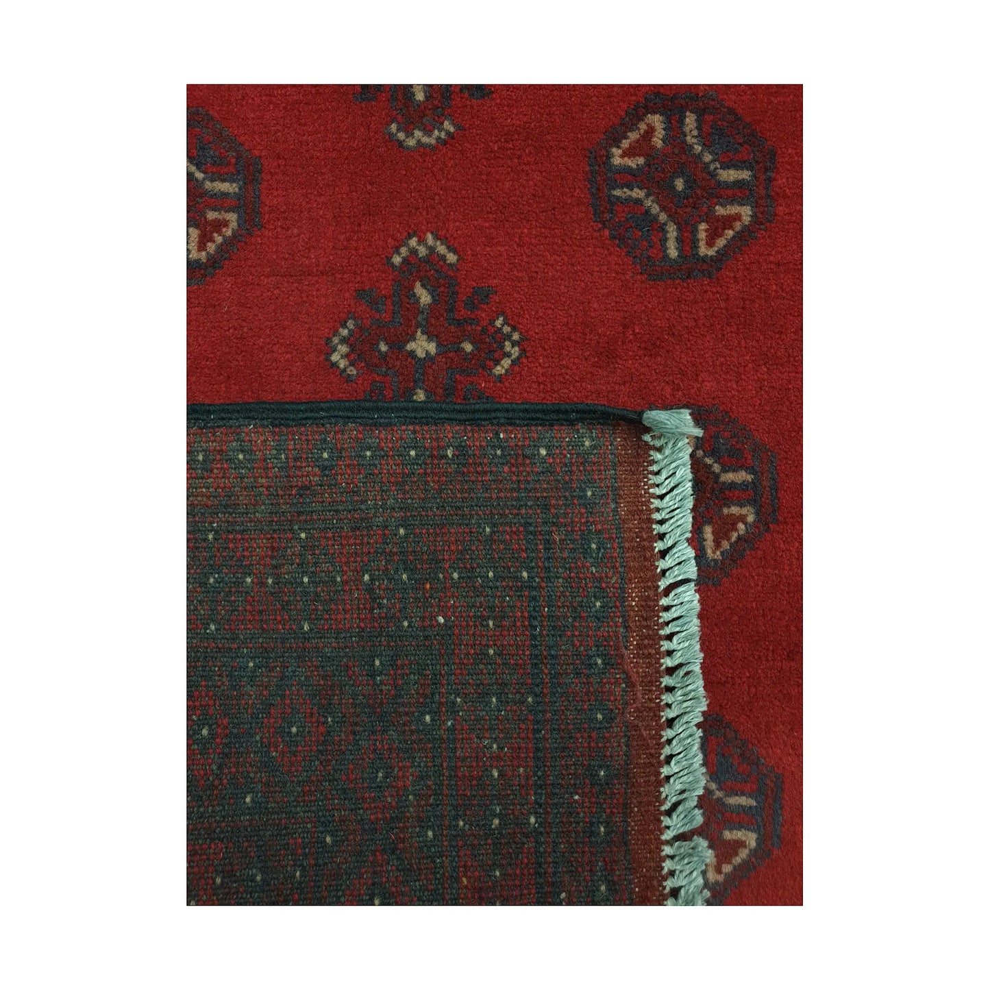 Folded corner detail of Afghan Turkoman rug showing the back of the rug, fringe and red front pattern