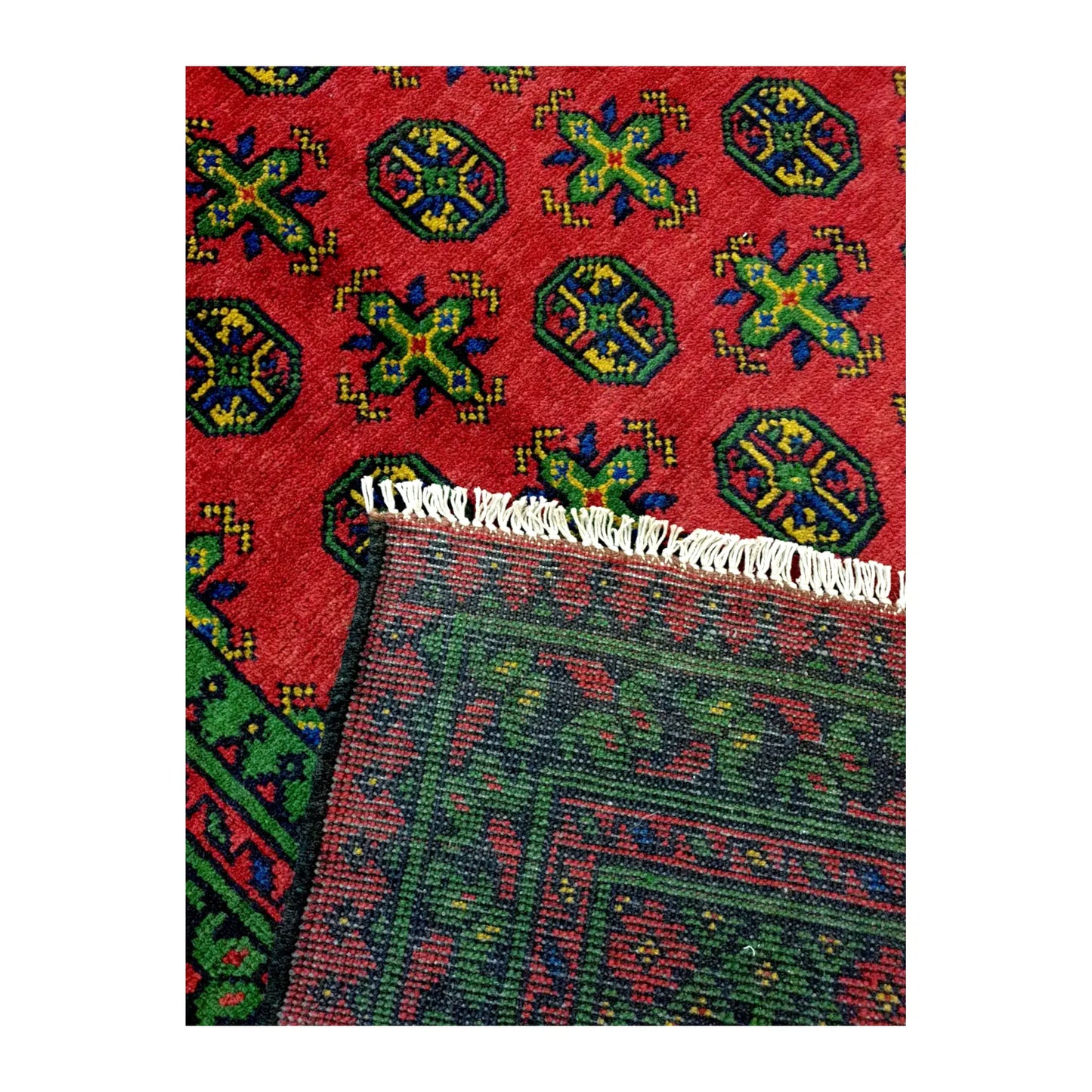 Folded corner of Afghan Turkoman rug showing the patterned face, reverse weave and ivory fringe