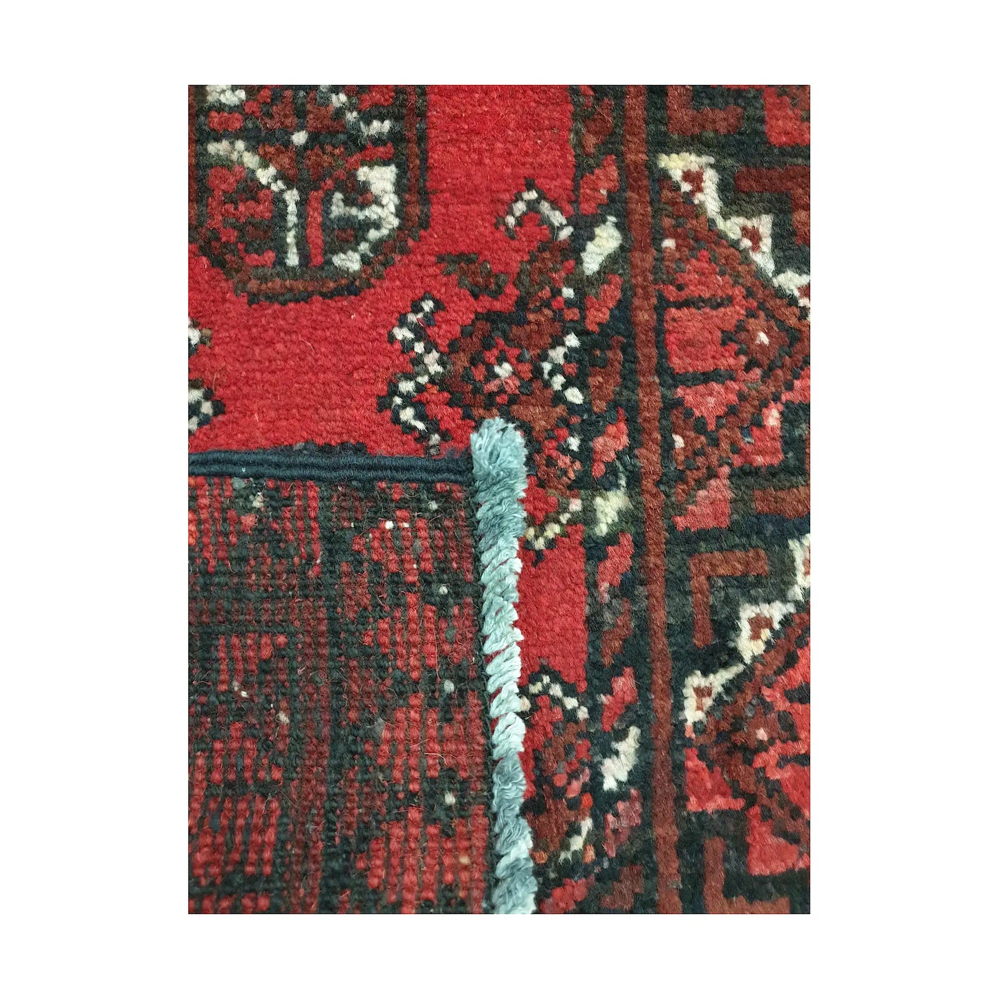Folded corner detail of Afghan Turkoman wool rug showing the back, fringe and red front pattern