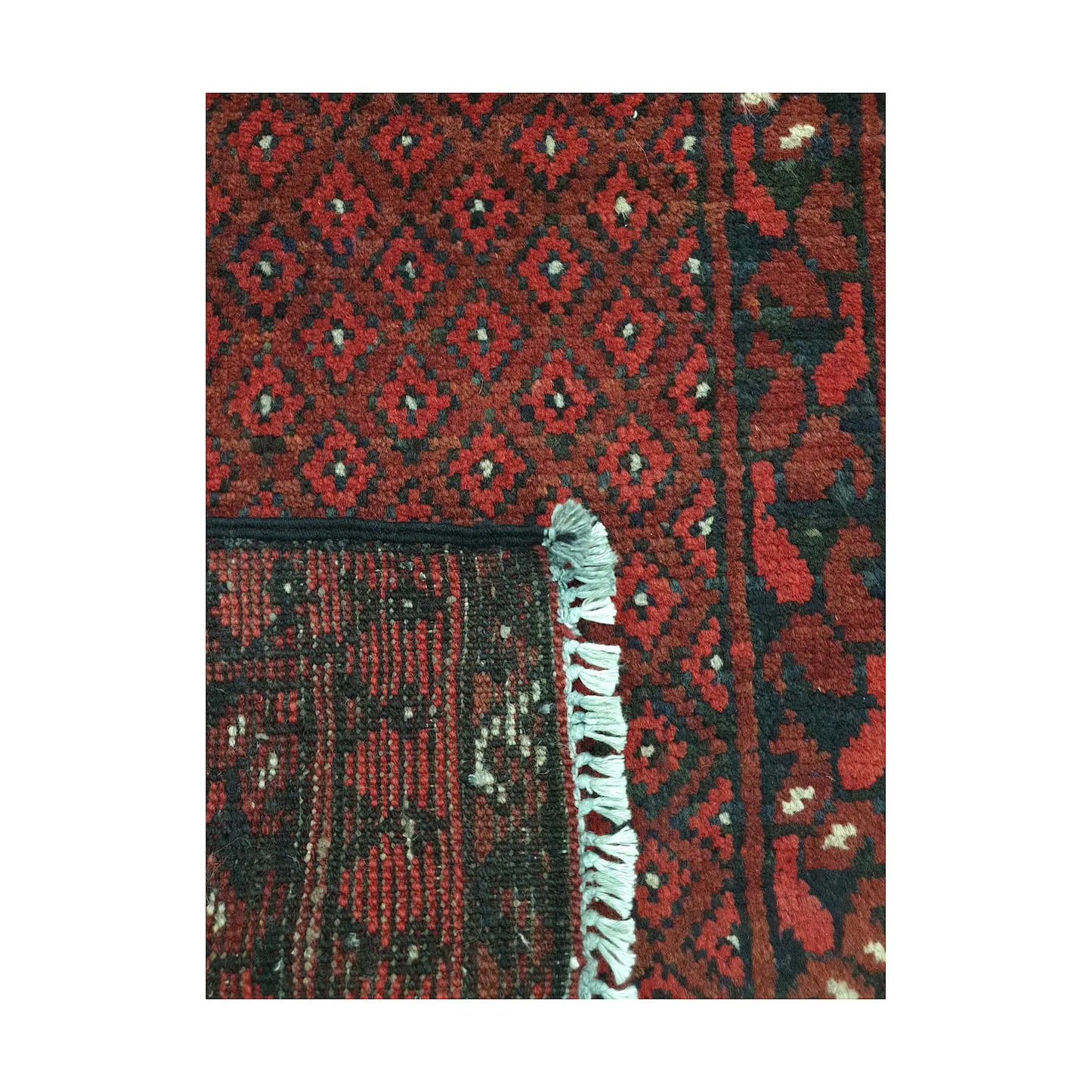 Folded corner detail of Afghan Turkoman wool rug showing the back, fringe and red patterned surface