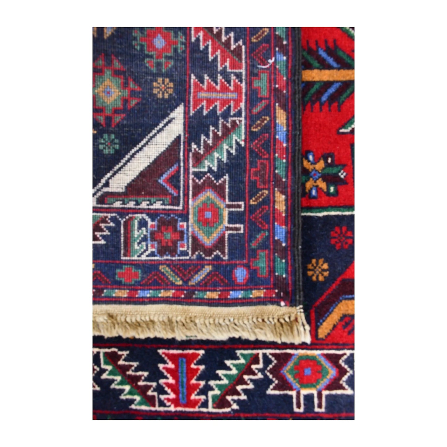 Folded corner of Baluchi runner showing the patterned face, reverse weave and fringed finishing edge