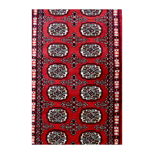 Length field detail of Bokhara wool runner rug showing repeated oval gul-style motifs and geometric border