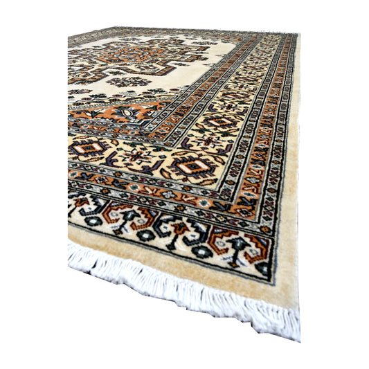 Angled view of Jaldar wool rug showing its warm beige field, central medallion, multicoloured borders and white fringe