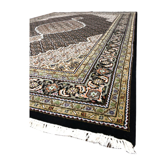 Angled view along the Mahi Tabriz rug showing its dark patterned field, layered floral borders and white fringe
