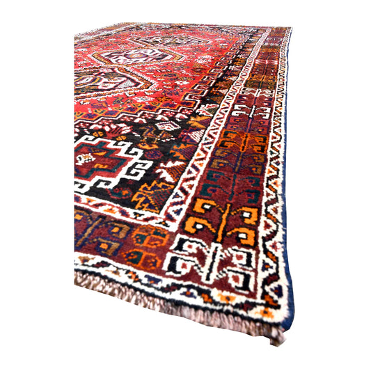 Angled detail of Persian Shiraz wool rug showing its red field, geometric motifs, layered side border and wool pile