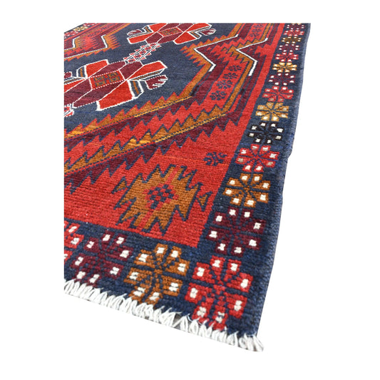 Angled view of red Baluchi wool rug showing its geometric field, patterned border and pale fringe