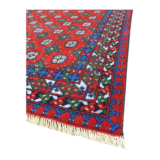 Angled view of Turkoman rug showing its red gul field, blue and green patterned borders and pale fringe