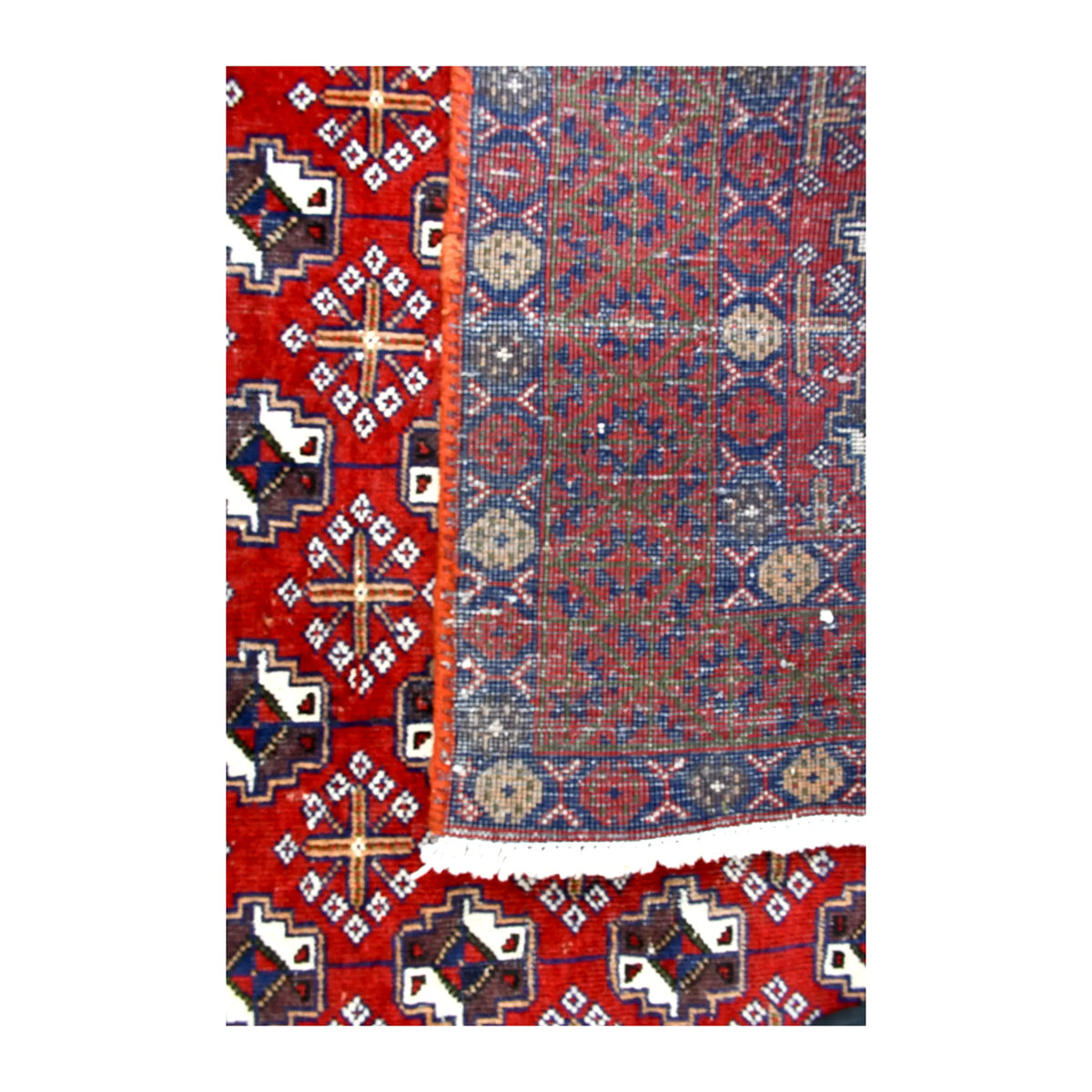 Folded-corner detail of Persian Turkoman rug showing the reverse weave, red geometric front and pale fringe