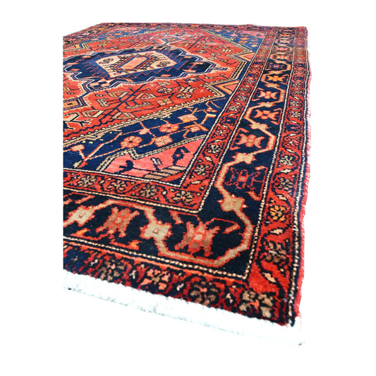 Angled view of Persian Zanjan rug showing its brick-red field, navy medallion, patterned borders and pale fringe
