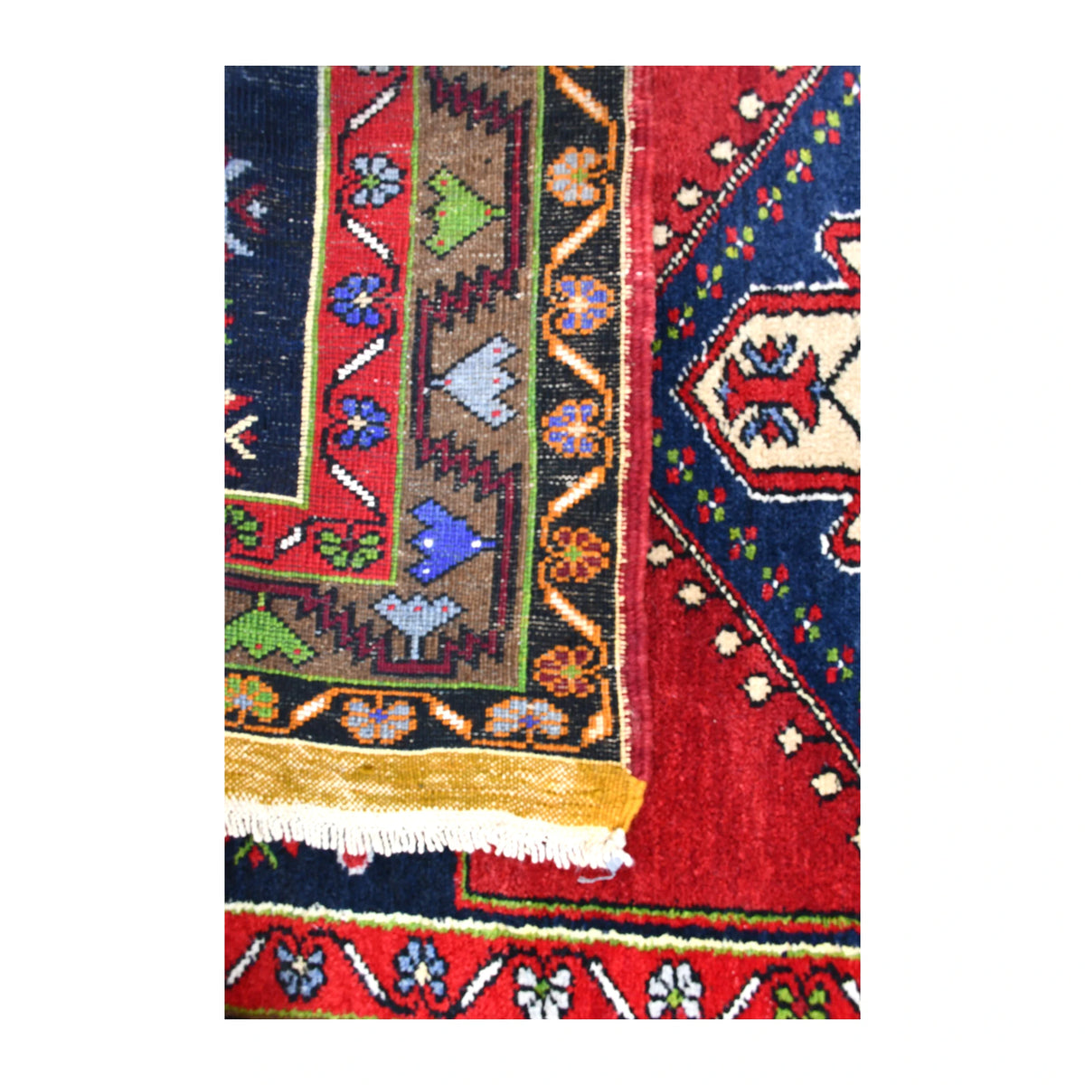 Folded-corner detail of vintage Yahyali rug showing the reverse weave beside its red and navy front and white fringe