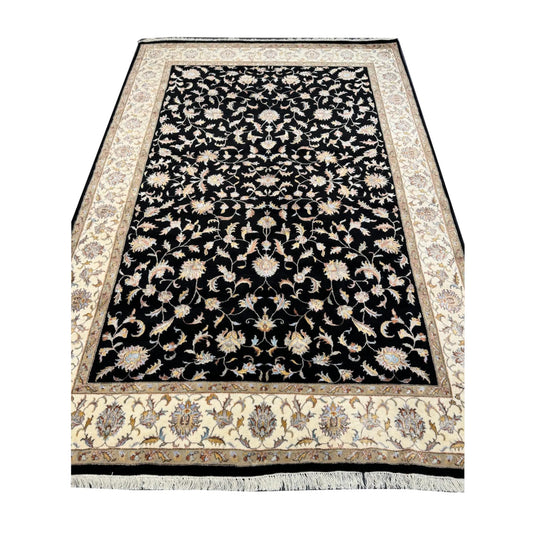 Fringe-end perspective view of black Ziegler rug showing the floral field and beige border