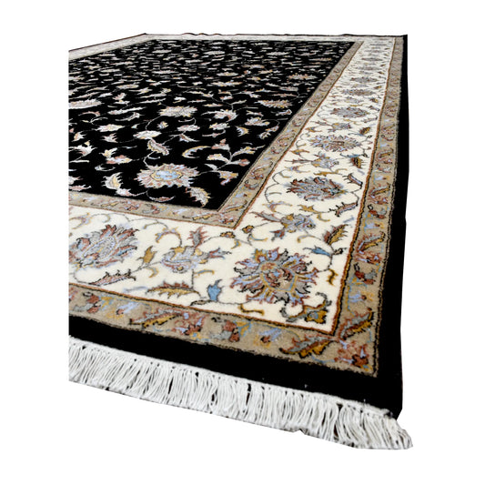 Angled view of black Ziegler rug showing its floral field, cream patterned border and white fringe