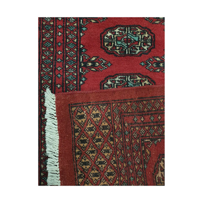 Folded corner detail of Afghan Bokhara runner rug showing the back of the rug, fringe and red front pattern