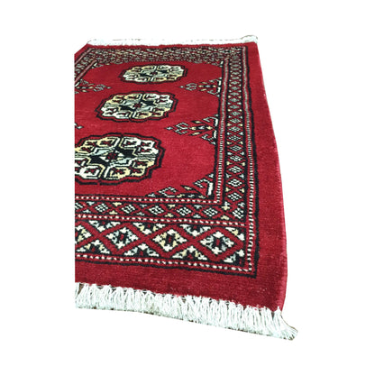 Angled fringe and border detail of Afghan Bokhara wool rug showing red pile, ivory gul motifs and dark geometric edging