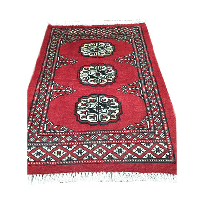 Red field and border detail of Afghan Bokhara wool rug showing three ivory gul medallions and traditional border pattern