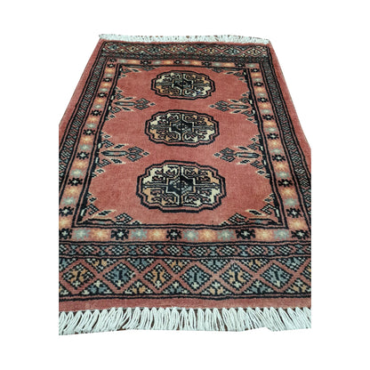 Salmon red field and border detail of Afghan Bokhara wool rug showing three ivory gul medallions and geometric border